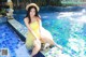 A woman in a yellow dress sitting on the edge of a swimming pool.