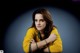 A woman in a yellow sweater leaning on a table.