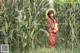 A woman in a red dress and straw hat standing in a corn field.