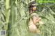 A naked woman sitting in a field of tall grass.