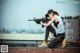 A woman sitting on top of a building holding a rifle.