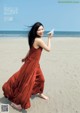 A woman in a red dress holding a paper airplane on the beach.